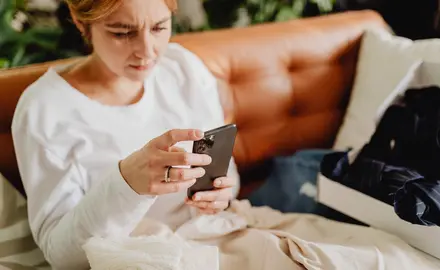 A woman sits on a sofa glaring at her phone.