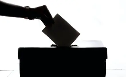 A silhouette of a hand dropping a ballot in a ballot box.