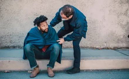 A public safety officer helps a man sitting on a curb.