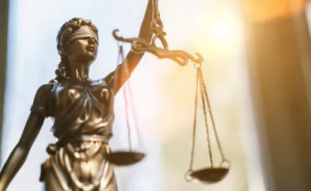 A photo of a statue of lady justice holding scales with sunlight in the background.