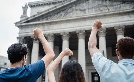 Three people raise their fists outside the Supreme Court building.