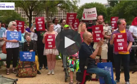 A group of people standing outside holding signs that read "Not Above the Law"