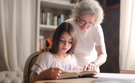 A grandmother helping her granddaughter read a book.