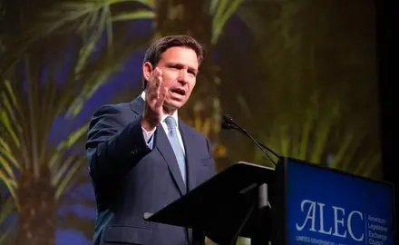 Ron DeSantis standing in front of a podium that says "ALEC" on it.