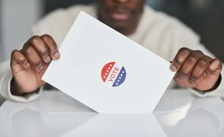 Two hands holding a piece of paper with a sticker that says "Vote"