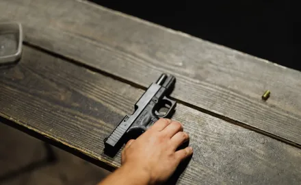 A hand setting a gun on a wooden table.
