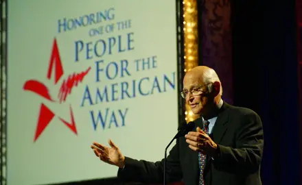 Norman Lear at a podium in front of a sign that reads "People For the American Way"