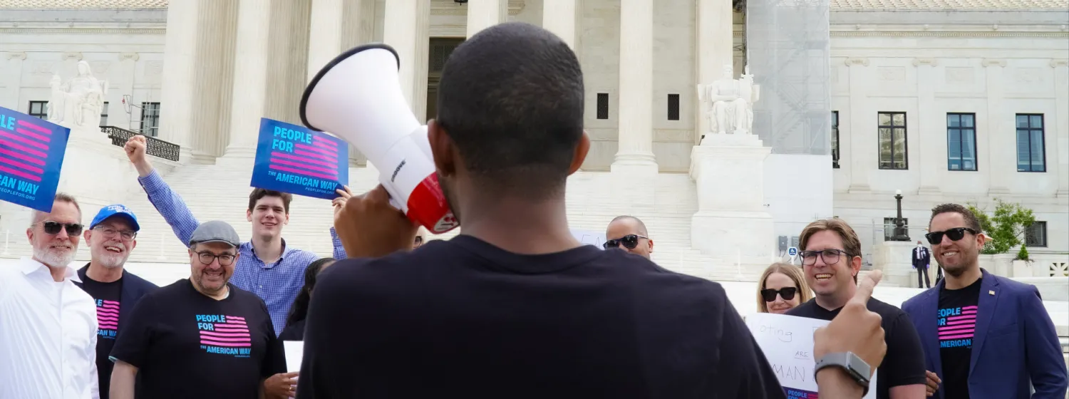 People holding signs that say "People For the American Way" in front of the Supreme Court