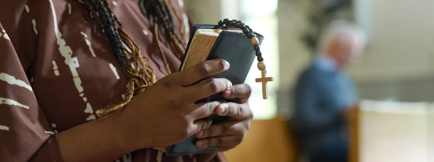 Black woman holding a bible with a cross bookmark 