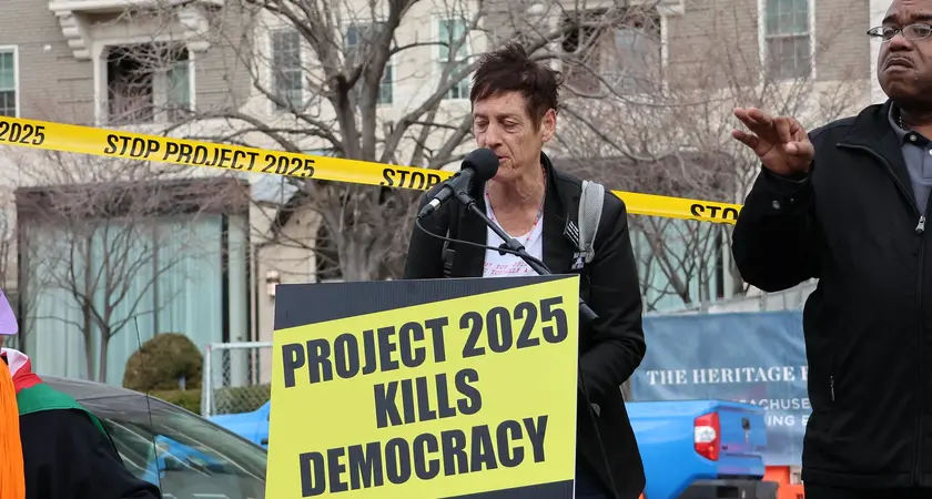 Rally speaker in front of a sign that reads "Project 2025 kills democracy"