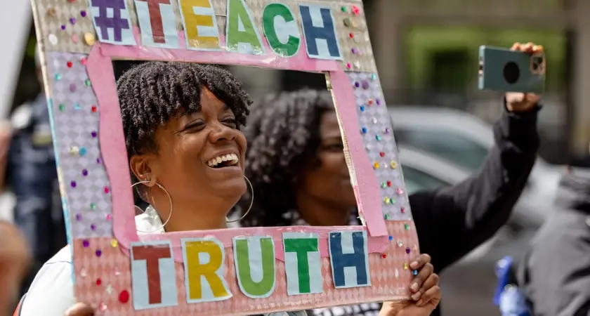 Woman holding a sign framing her face  that says #TeachTruth