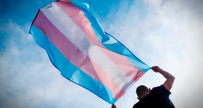 A man holds the transgender flag above his head.