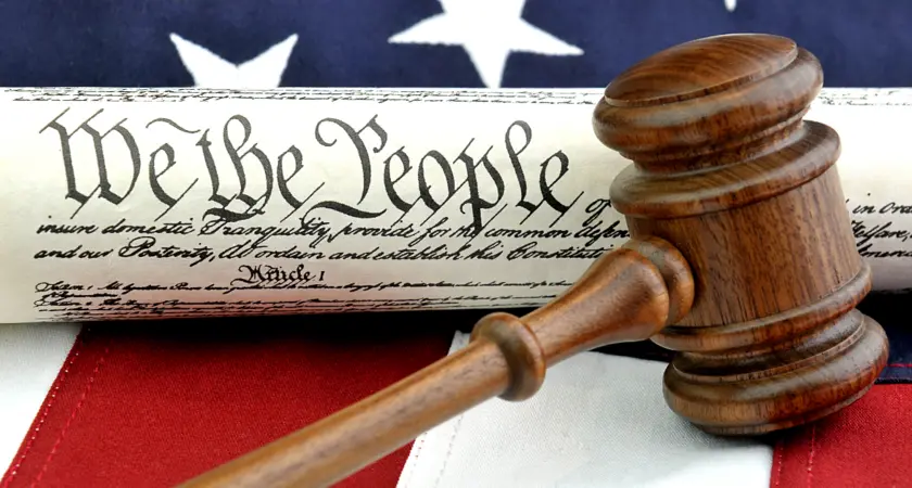 Picture of an American Flag and the U.S. Constitution with the phrase "We The People" clearly visible underneath a gavel.