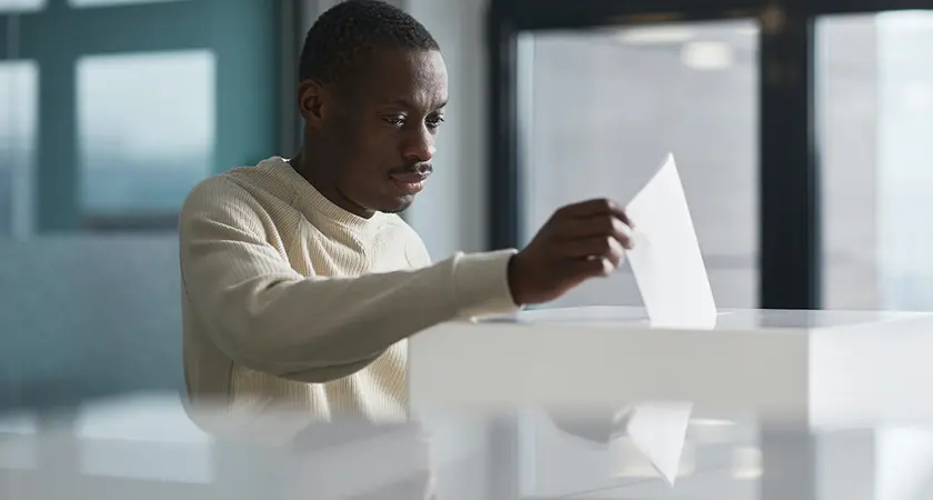 A black man deposits a ballot into a voting box.