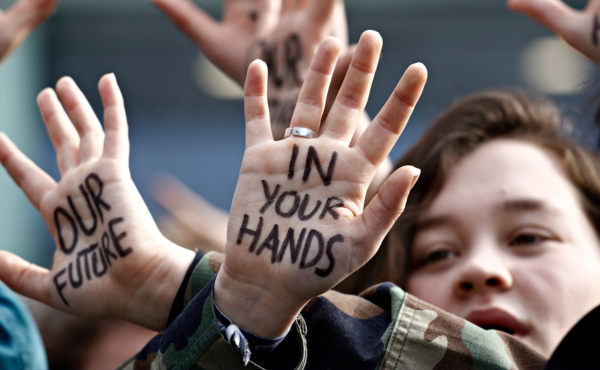 A young woman holds her hands to the camera. Written on them is "our future is in your hands"
