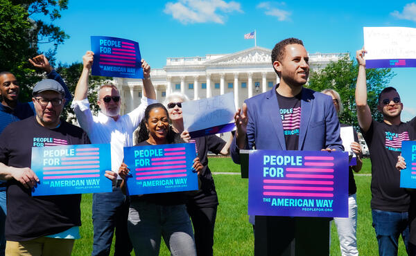 A group of people outside the Supreme Court building hold signs.