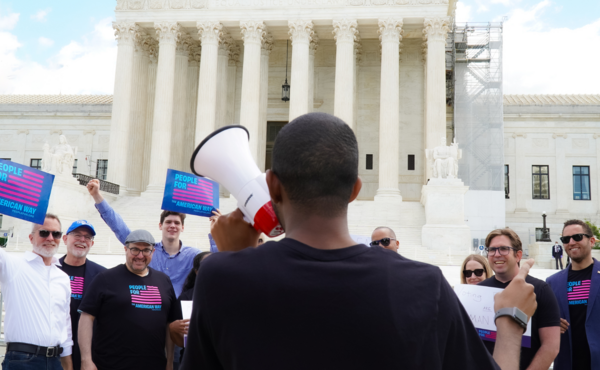 People holding signs that say "People For the American Way" in front of the Supreme Court