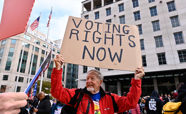 Older man holding a sign at a protest that reads "voting rights now!" 