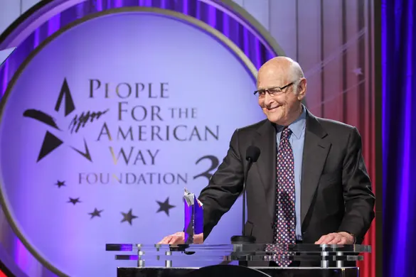 Norman Lear standing at a podium in front of a People For the American Way banner