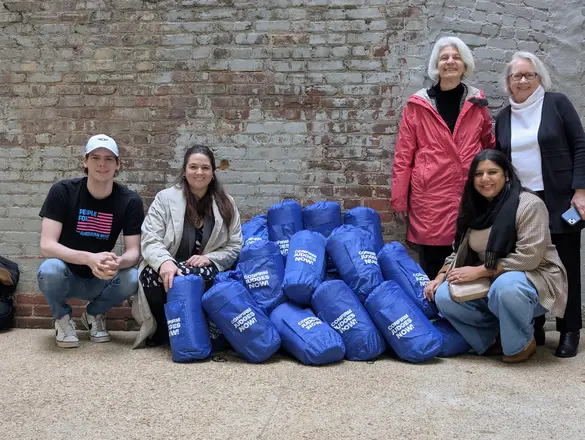 A group of people posing with a pile of sleeping bags by a brick wall