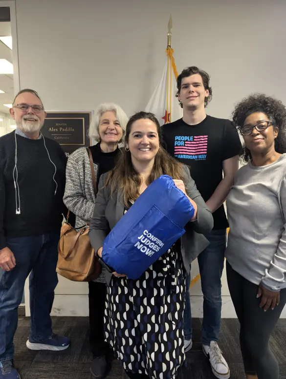 five people stand outside a senator's office. one holding a sleeping bag that reads "confirm judges now"