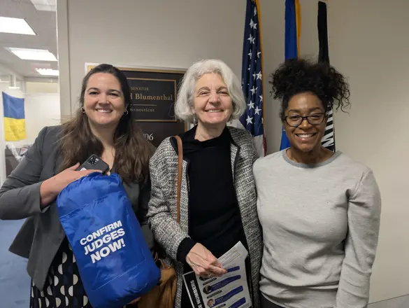 three people pose with a sleeping bag that says "confirm judges now" on it