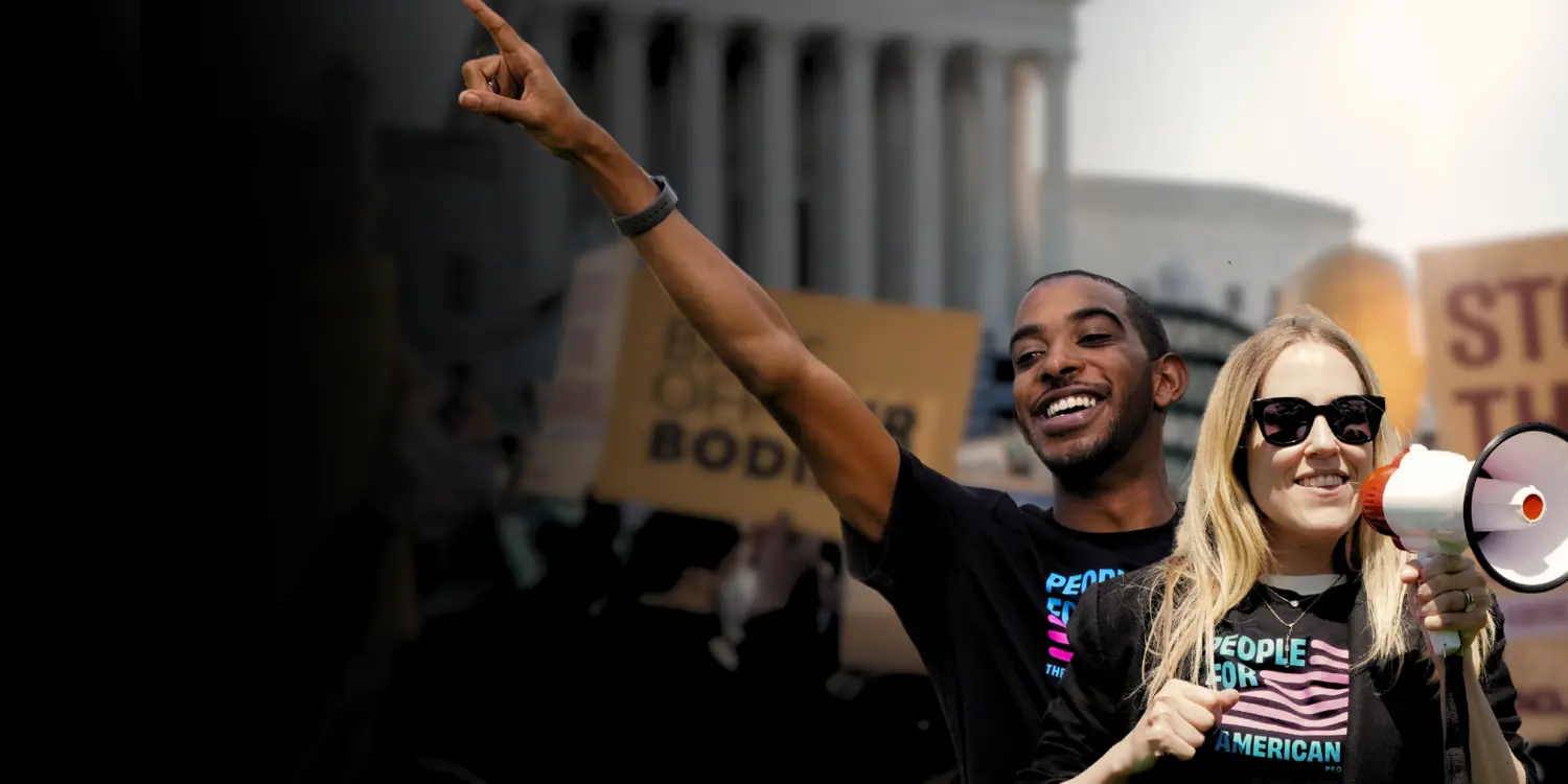 a white woman holding a megaphone and a Black man pointing to the sky at a rally