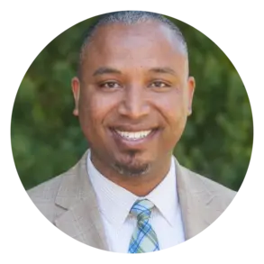 Photo of Rev. Michael Ray Matthews, a smiling BLack man in a tan suit and plaid tie on a green background