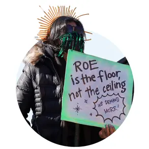 Woman holding a sign that says "Roe is the floor, not the ceiling. We demand more." 