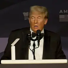 Donald Trump in a tuxedo speaks at a lectern in front of logos for the America First Policy Institute and its political arm, America First Works.