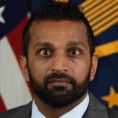 Kash Patel pictured in front of an American flag staring intensely at the camera