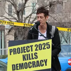 Rally speaker in front of a sign that reads "Project 2025 kills democracy"