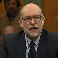 Russ Vought, in suit and tie, seated and speaking into a microphone.