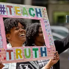 Woman holding a sign framing her face  that says #TeachTruth