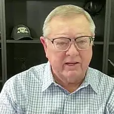 Image of Tim Sheets, a post-middle-age white man wearing glasses, sitting with bookshelf behind him  