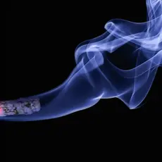 A cigarette releasing smoke in front of a black background