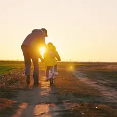 Dad teaching a daughter to ride a bike on a dirt road