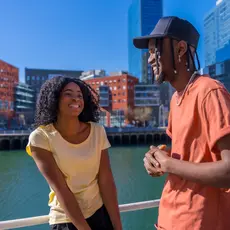 Photo of a young Black man and woman walking along a body of water in a city