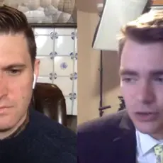 Nick Fuentes stands in front of American flag with a Trump campaign hat on