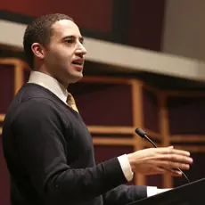 Photo of Svante Myrick wearing a black sweater and speaking in front of a podium.