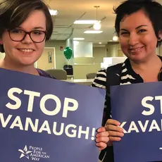 Two smiling students hold blue signs that say Stop Kavanaugh.