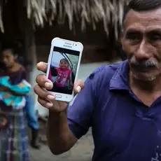 A man holds a cell phone with a picture of a young girl