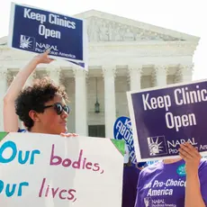 A group of people stand in front of the Supreme Court building with signs that say "Our bodies, our lives" and "Keep clinics open."