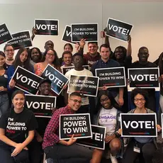 A group of people holding signs that say "Vote" and wearing tee-shirts that say "I'm building the power to win!"