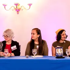 A group of multicultural women sit on a panel.