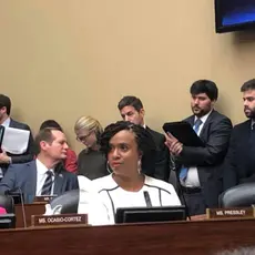 Rep. Ocasio-Cortez and Rep. Ayanna Pressley sit in a room during a hearing