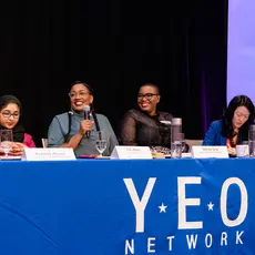 Six women sit on a panel behind a table with a banner that says "YEO Network"