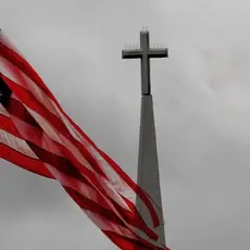 An American flag waves in front of the steeple of a church that is topped with a cross