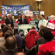 A group of people hold pro-Medicare signs in the senate.