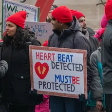 A group of anti-abortion protesters wearing red hats and holding signs that say "Heartbeat detected, must be protected"